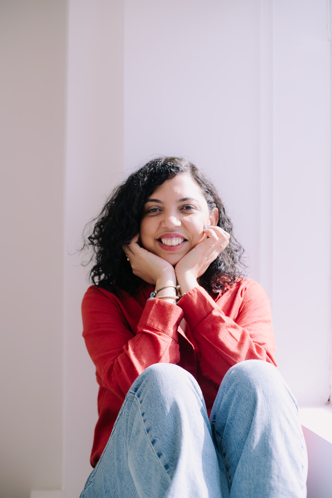 Retrato espontâneo de Nangela Lima sorrindo junto à janela